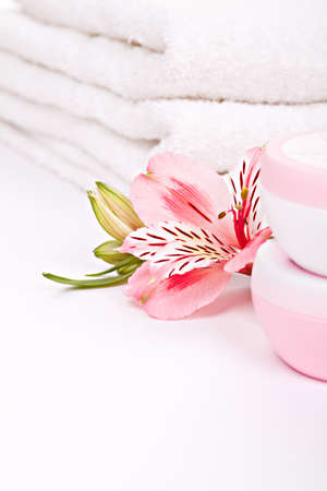 Alstroemeria pink flowers with moisturizing cream against stack of towelsの写真素材