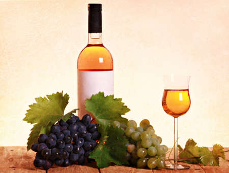 A bottle of white wine with grapes and leaves on wooden backgroundの写真素材