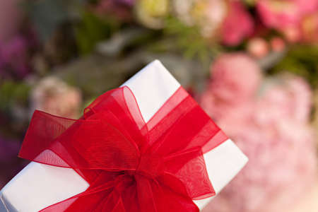 Closeup gift box with red bow on flowers background