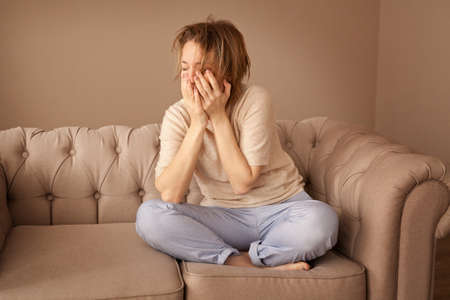 Sad depressed woman at home sitting on sofaの写真素材