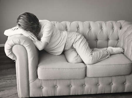Sad depressed woman at home sitting on sofa