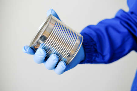 Canned food in a hand in a glove on a white background.Concept: coronavirus, quarantine, economy