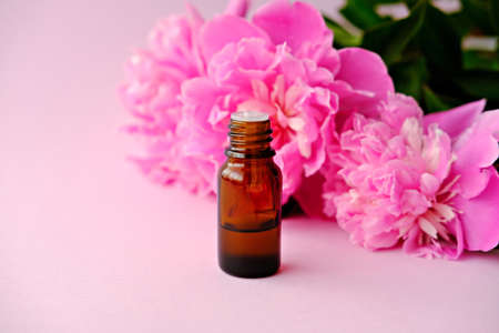 Bottles of essential oil and pink peonies flowers