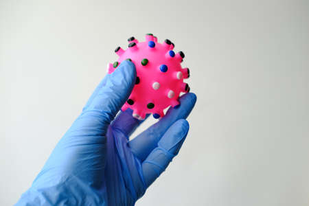Ðuman hand in a glove holds the covid virus on white background. Concept design with red ballの写真素材