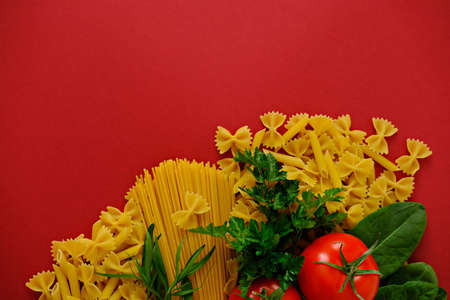 Uncooking pasta with tomatoes and fresh herbs on red background