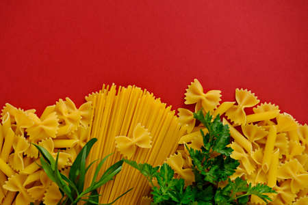 Uncooking pasta with tomatoes and fresh herbs on red backgroundの写真素材