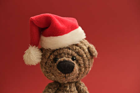 Cute portrait of knit handmade bear toy in Santa's hat on red christmas backgroundの写真素材