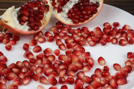 Pomegranate seeds and broken fruits on a white plateの写真素材