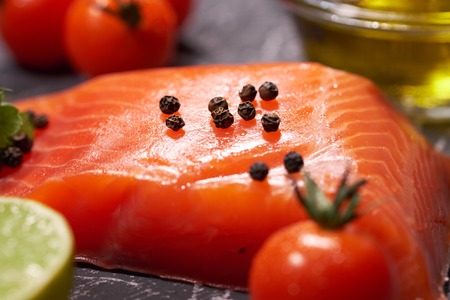A piece of salmon on a gray background, tomatoes, dill, olive oil, lemon. Selective focus, space for...