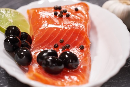 A piece of salmon on a white plate with olives and lemon, on a gray background. Selective focusの写真素材
