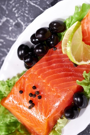 A piece of salmon on a white plate with olives and lemon, on a gray background. Selective focusの写真素材