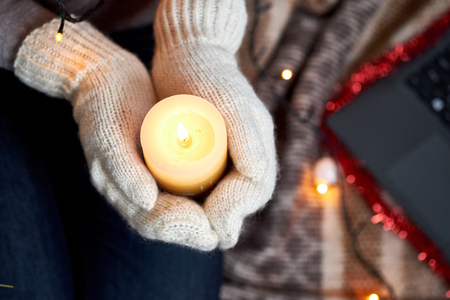 Candle in hands in mittens. Christmas garland and plaid on the background.の写真素材