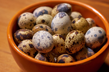 Quail eggs in clay bowl on brown wooden backgroundの写真素材