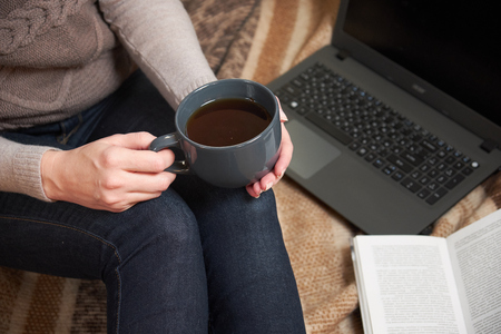 Woman with a Cup of tea, a book,  mittens and a laptop on a blanket.の写真素材