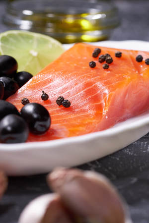 A piece of salmon on a white plate with olives and lemon, on a gray background.の写真素材