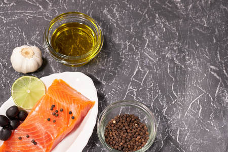 A piece of salmon on a white plate with olives and lemon, on a gray background. Selective focus,の写真素材