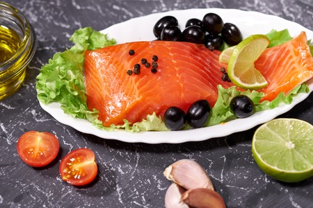 A piece of salmon on a white plate with olives and lemon, on a gray background.の写真素材