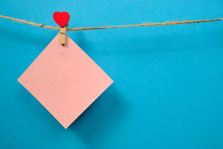 Pink  paper for notes  on the clothespin with hearts  on a blue background. Close upの写真素材