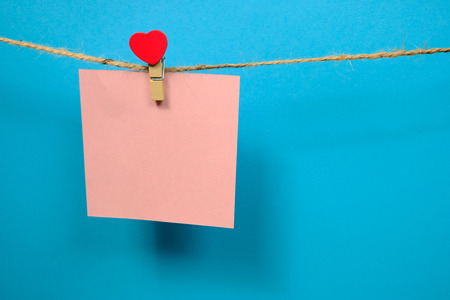 Pink  paper for notes  on the clothespin with hearts  on a blue background. Close upの写真素材