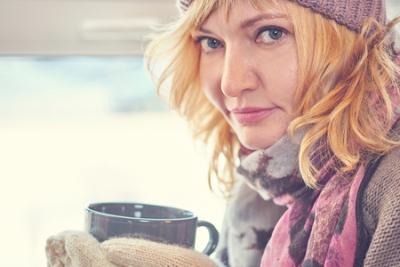 A woman in a wool cap and sweater with a Cup of tea looking out the window.の写真素材