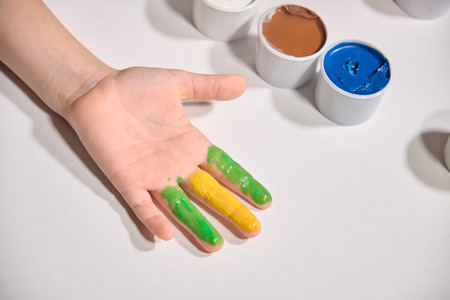 Little girl paints her hands with finger paint on white background. Bright coloursの写真素材