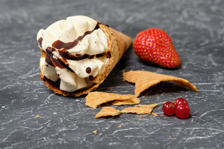 vanilla ice cream in waffle cone with chocolate icing on dark grey background with strawberry . Close upの写真素材