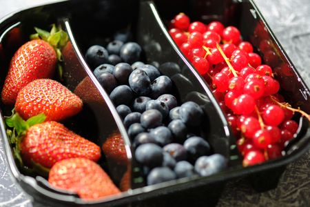 plastic containers box of berries, red currants, blackberries, and strawberries on the grey backgroundの写真素材