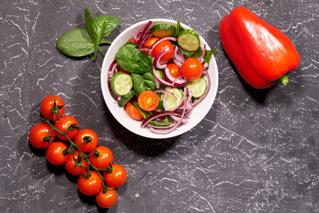 Vegetable salad in a white plate on a gray background, next to the Bulgarian pepper, tomatoes, spinach.の写真素材