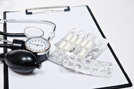 phonendoscope and tonometer  with a folder with white sheets of paper and pills  on a white background. Close upの写真素材
