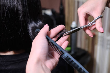 Hairdresser makes a hairstyle brunette  girl  in a beauty salon with scissors and comb . Close upの写真素材
