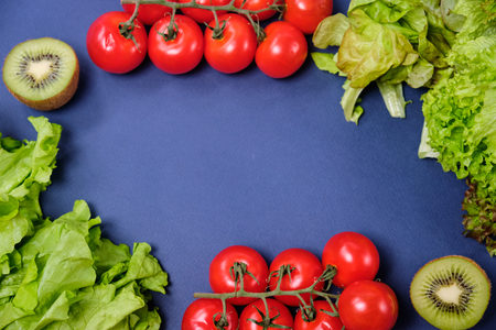 fresh vegetables and fruits on dark blue background. Lettuce, cherry tomatoes, half lemon and kiwi. Copy spaceの写真素材