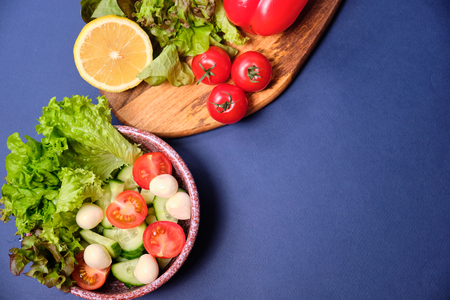 fresh vegetables and a bowl of salad with mozzarella on a blue background. The ingredients for a Caprese salad . Lettuce, cherry tomatoes, mozzarella, lemon. Copy spaceの写真素材
