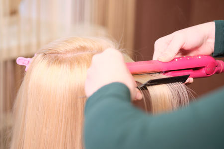 Hairdresser makes a hairstyle blonde girl  in a beauty salon with Curling iron. Close upの写真素材
