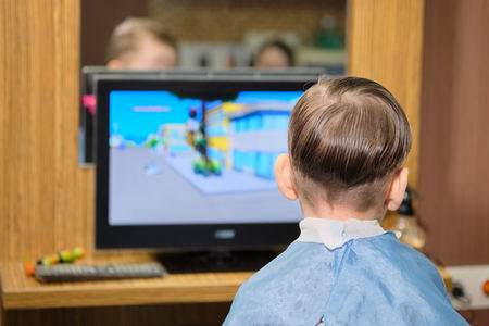 Barber shop. Hairdresser makes hairstyle to a  boy .  Boy watching a cartoonの写真素材