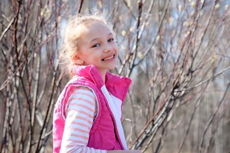 Portrait of a girl in a red vest in early spring on the background of willowの写真素材