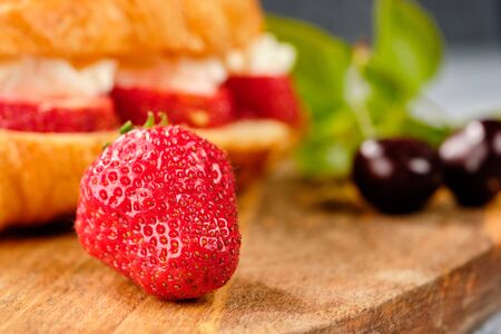 croissant sweet sandwich with cream cheese and strawberries on a wooden board and gray background. Useful breakfast. Proper nutrition. French traditional dishes. Close upの写真素材