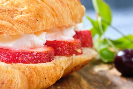 croissant sweet sandwich with cream cheese and strawberries on a wooden board and gray background. Useful breakfast. Proper nutrition. French traditional dishes. Close upの写真素材