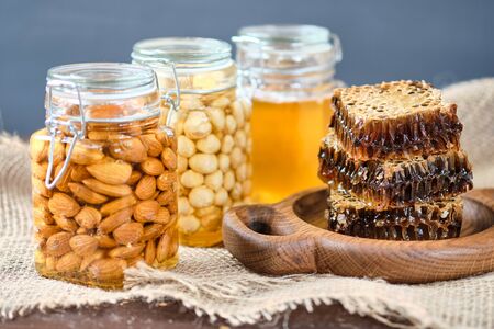honey in honeycombs on a wooden plate. Jars with honey and almonds and hazelnuts with lemon and ginger in the backgroundの写真素材