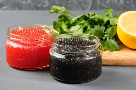black and red caviar in glass jars with parsley and lemon on a gray background. Russian national cuisineの写真素材