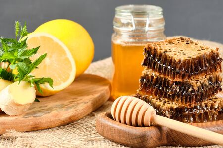 honey in honeycombs on a wooden plate and honey with nuts with lemon and ginger in rustic style on a wooden background. Close-upの写真素材