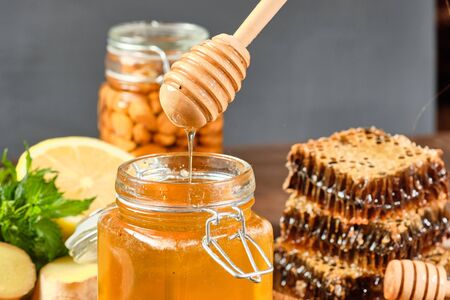 honey in honeycombs on a wooden plate and golden honey in a jar with nuts and comb for honey with lemon and ginger on a brown wooden backgroundの写真素材