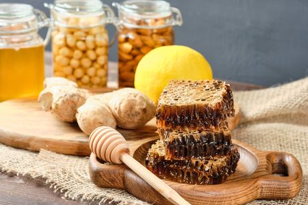 honey in honeycombs on a wooden plate. Jars with honey and almonds and hazelnuts in the backgroundの写真素材