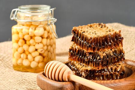 honey in honeycombs on a wooden plate and golden honey in jars with nutsの写真素材