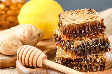 honey in honeycombs on a wooden plate. Jars with honey and almonds and hazelnuts in the backgroundの写真素材