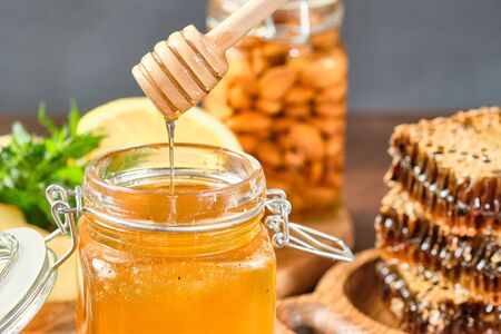honey in honeycombs on a wooden plate and golden honey in a jar with nuts and comb for honey with lemon and gingerの写真素材