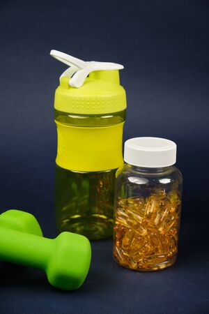 Plastic shaker, green dumbbells and a can of omega 3 on a blue backgroundの写真素材
