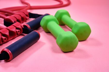 Fitness equipment, green dumbbells and a rubber expander with black handles on a pink background,の写真素材