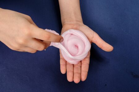 Pink slimy toy in the hands of children on a blue background. Make slime. Copyspace. Flatley.の写真素材