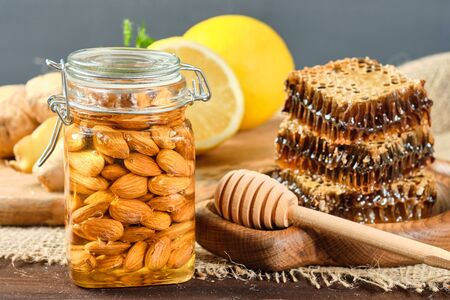 honey in honeycombs on a wooden plate and honey with nuts with lemon and ginger in rustic style on a wooden background. Close-upの写真素材