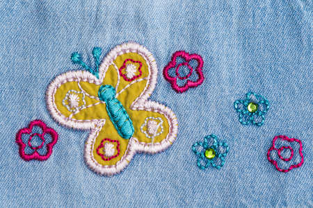 Fragment of the denim fabric with embroidery in the form of flowers and butterfliesの写真素材